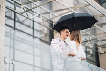 Young couple of lovers under a umbrella in city. Handsome people having fun in city urban center in a raining day. Love and vacation concept