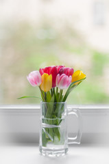piccoli tulipani colorati su una finestra bianca in una tazza di vetro
