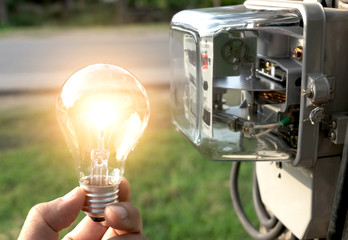 hand of person holding light bulb from outdoor with watt hour meter beside.