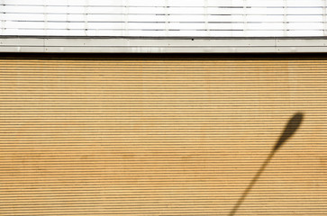 Coupled lamppost casts a shadow on vinyl sidings of a building's wall.