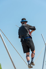 Obraz premium rear view of Street performer walking tight rope and playing violin in an unusual way