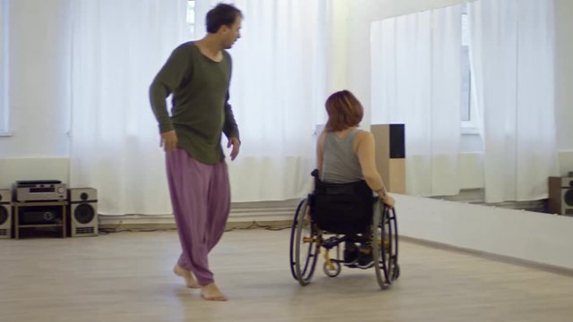 Positive woman in wheelchair dancing with male choreographer in studio while having recovery therapy