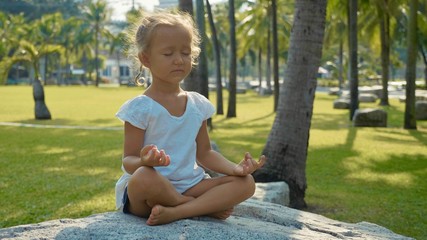 Little child girl meditating in beautiful park with palm trees on the background