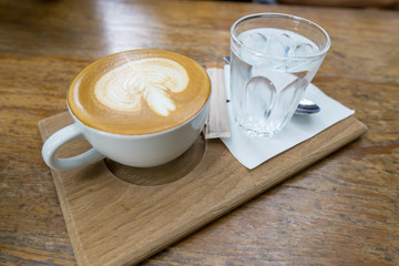 Hot coffee latte in white cup with water in a glass on the wooden table in coffee shop., holiday concept.