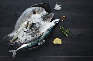 Fresh fish with ice in ceramic tray on dark wooden background. Flat lay. Top view