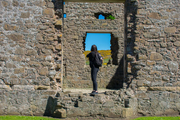 back view on woman with backpack standing on stone wall old ruins of medieval castle. tourism concept  