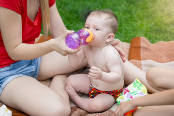 Cute baby boy sitting on blanket on family picnic and drinking juice from bottle