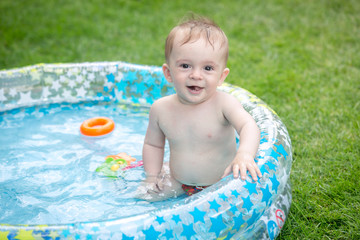 Fototapeta na wymiar Portrait of cheerful smiling baby boy sitting in inflatable swimming pool at garden