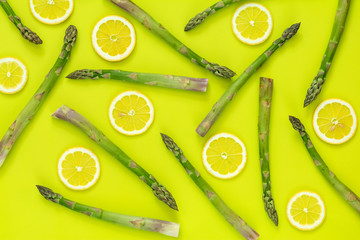 Asparagus sprouts and sliced lemon on bright green surface.