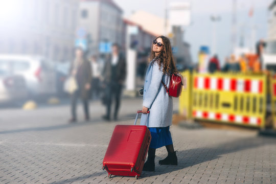  female traveler walks the city with a red suitcase.