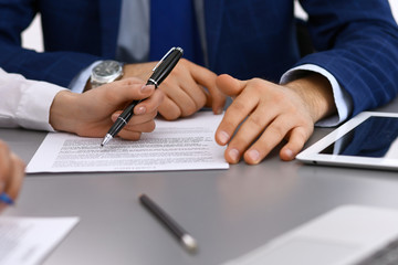 Group of business people and lawyer discussing contract papers sitting at the table, closeup. Businessman is signing document after agreement done