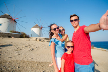 Family taking selfie with a stick in front of windmills at popular tourist area on Mykonos island, Greece