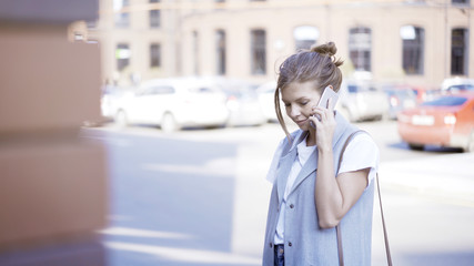 A young smiling pretty girl dressed in a jacket is having a call outside outdoors