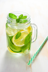 Detox water infused with sliced lemon, cucumber and sprigs of mint on wooden background.