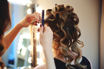 Hairstylist combs client's light-brown with blonde hair. Creating a luxurious evening hairstyle...