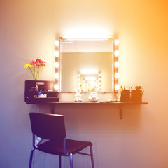 Working place of make up artist. Square mirror with lamps and rose bouquet in glass vase on empty shell for cosmetics.