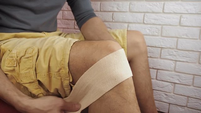 Sick knee. A man puts on an elastic bandage.