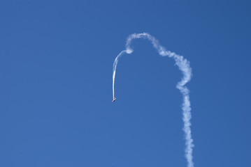 airplane dives down with a white smoke in blue sky