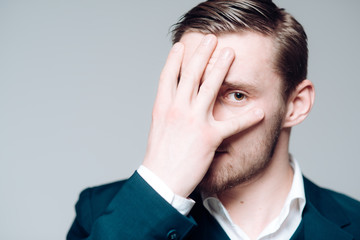 Blond model isolated on gray background. Bearded guy with hazel eyes covering his face with palm