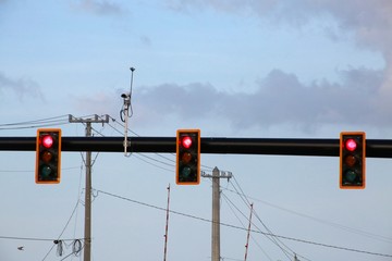 Three Red Traffic Lights against Thick White and Gray Fluffy Clouds with Power Lines in the...