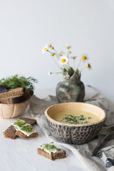 Cheese soup with mushrooms and vegetables, brown bread with butter, dill and basil on a white wooden background