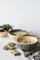 Cheese soup with mushrooms and vegetables, brown bread with butter, dill and basil on a white wooden background