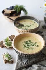 Cheese soup with mushrooms and vegetables, brown bread with butter, dill and basil on a white wooden background