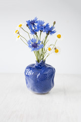 Bouquet of wild flowers in a blue vase on a white wooden background
