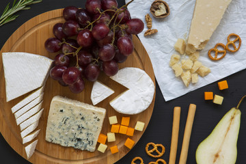 Fototapeta na wymiar Tasting cheese with fruits, pretzels walnuts and bread sticks on dark background. Food for wine, romantic. Top view. Flat lay.