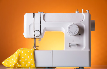Household electric sewing machine in work, on bright-orange