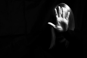 A woman hiding her face and showing gesture stop in a dark. Violence concept. Free space for your...