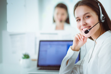 Smiling businesswoman or helpline operator with headset and computer at office