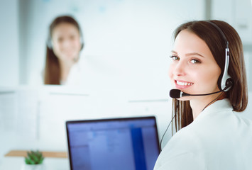 Smiling businesswoman or helpline operator with headset and computer at office
