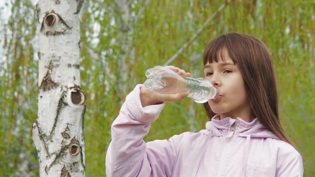 The child drinks water. A girl is drinking water in nature.