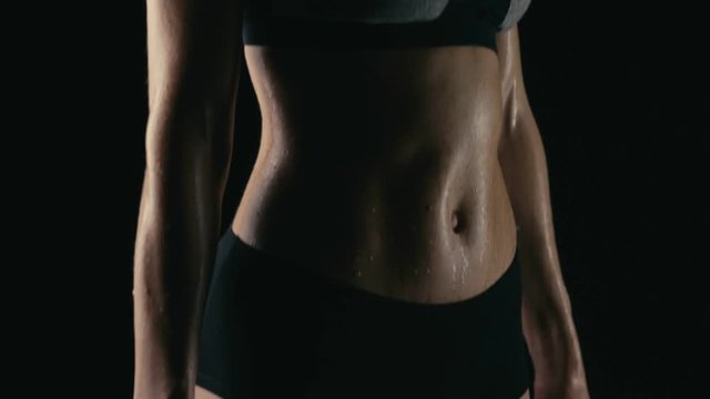 Young fitness blond woman with dumbbells breathing heavily on black background. Slow motion