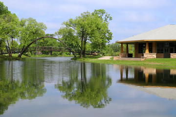 Fototapeta premium Beautiful summer landscape with a bridge, pavilion and fresh green color trees and grass around the lake Mendota bay in a Tenney Park, city of Madison, Wisconsin, Midwest USA.