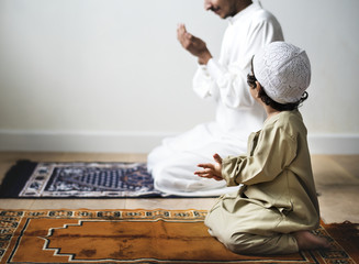 Fototapeta premium Little boy praying alongside his father during Ramadan