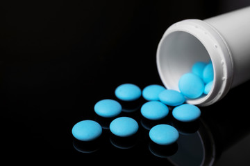 Container with blue pills on black background