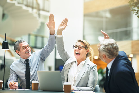 Mature businesspeople cheering and high fiving together in an of