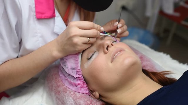 eyelash extension procedure - master and a client in a beauty salon