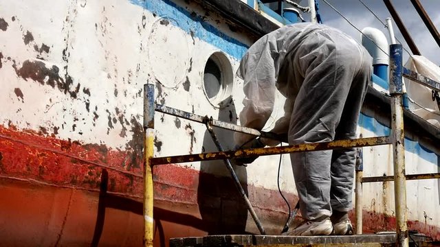 Working people tear off paint on metal in repairs process at shipyard. Workers in overalls reconstruct at ship repair yard outdoors in port. Slow motion.
