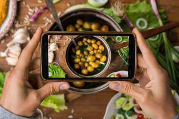 Phone photography of food. Woman hands take photo of lunch with smartphone for social media. Cooked new potatoes in pot with onion and olive oil or butter. Raw vegan vegetarian healthy dinner 