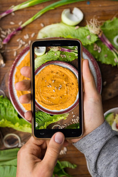 Phone photography of food. Woman hands take photo of lunch with smartphone for social media. Israeli hummus with chickpea, tahini, olive oil. Raw vegan vegetarian healthy dinner 