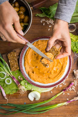 Woman hands spreads hummus on raw bread. Traditional Israel food - dip or spread with chickpea, tahini. . Served with vegetables Greek salad and greens. Raw vegan vegetarian healthy food