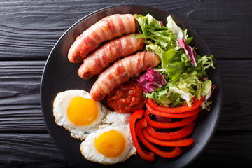 Breakfast Pigs in blankets fried sausages wrapped in bacon, eggs, sauce and fresh salad close-up. horizontal top view