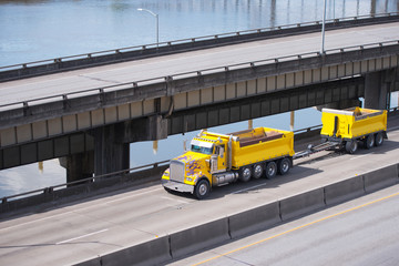 Big rig yellow tipper semi truck with dump trailer running on overpass intersection road along the...
