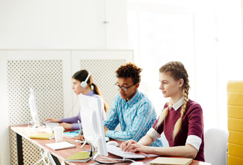 Row of young students of programming faculty sitting in front of computer monitors and learning at lesson