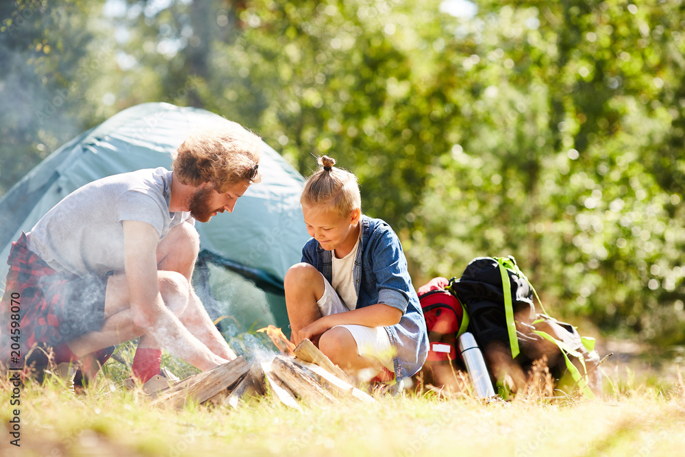 Wall mural Father and son burning campfire in natural environment during trip on summer day