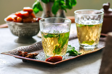 Traditional moroccan mint tea with dates on a vintage tray. White stone background.
