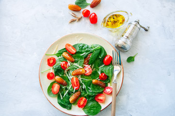 Fresh salad with spinach tomatoes cherry and dates served on a plate. White stone background. Healthy eating concept.